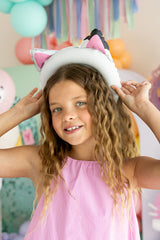 Young girl wearing a white cat hat with pink ears in a colorful room.
