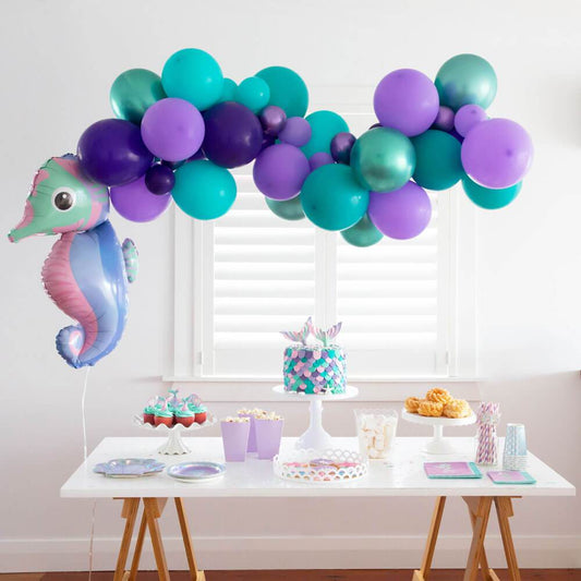 Mermaid party table with seahorse balloon, pastel cupcakes, cake, and purple teal balloon garland